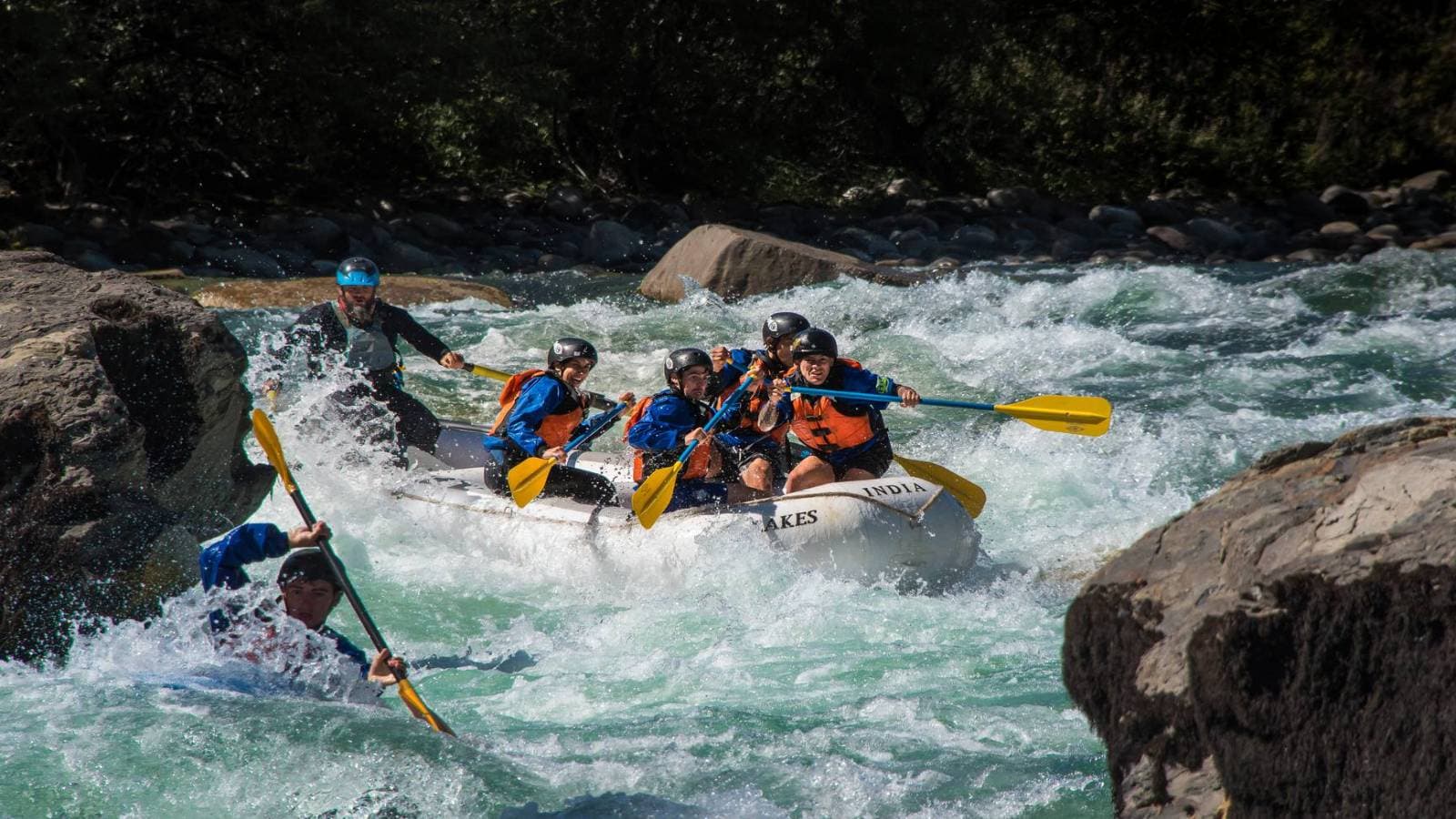 Personas remando en una balsa blanca a través de rápidos espumosos en un río boscoso.