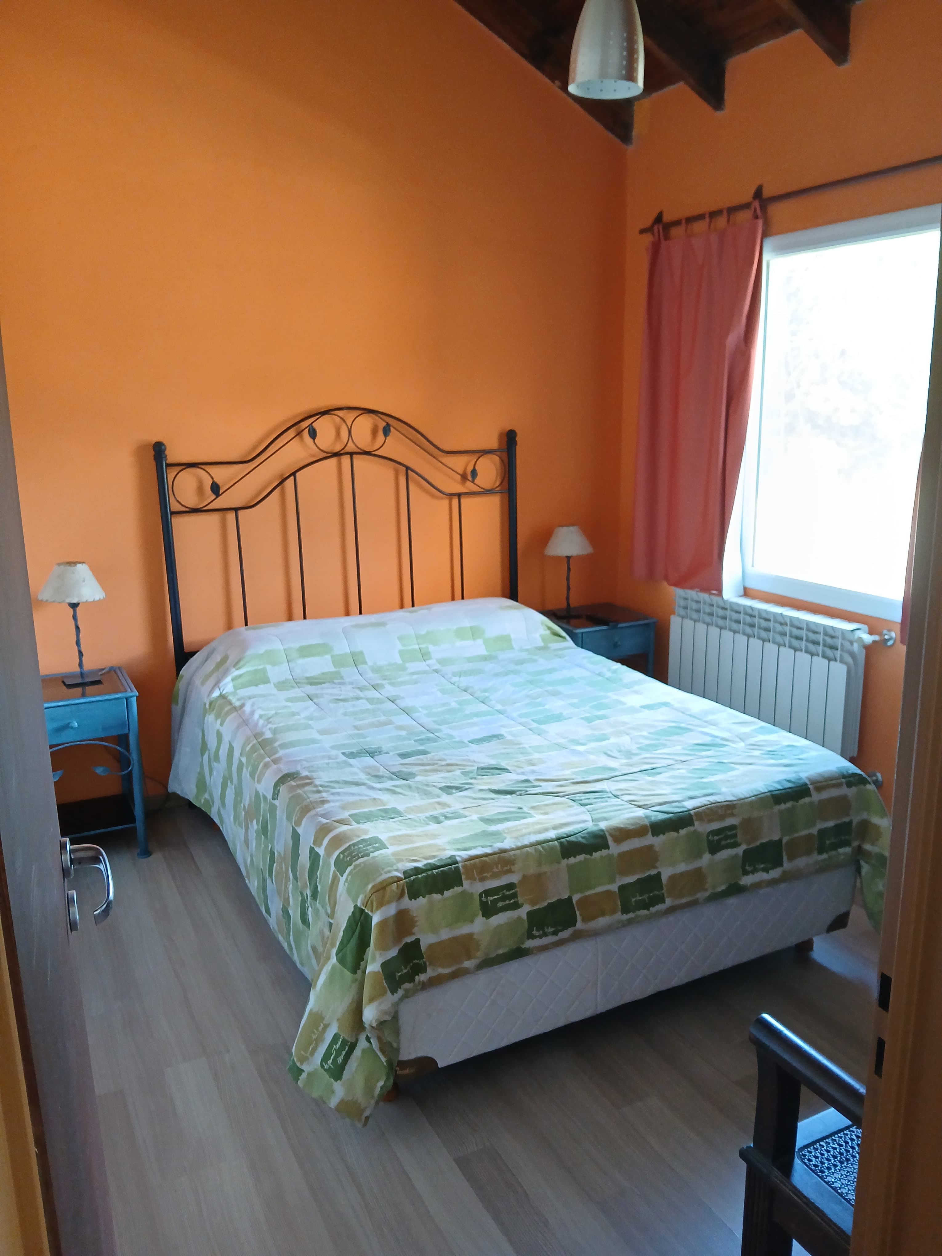 Dormitorio con paredes naranjas, cama con colcha de cuadros verdes y cabecero de hierro negro.