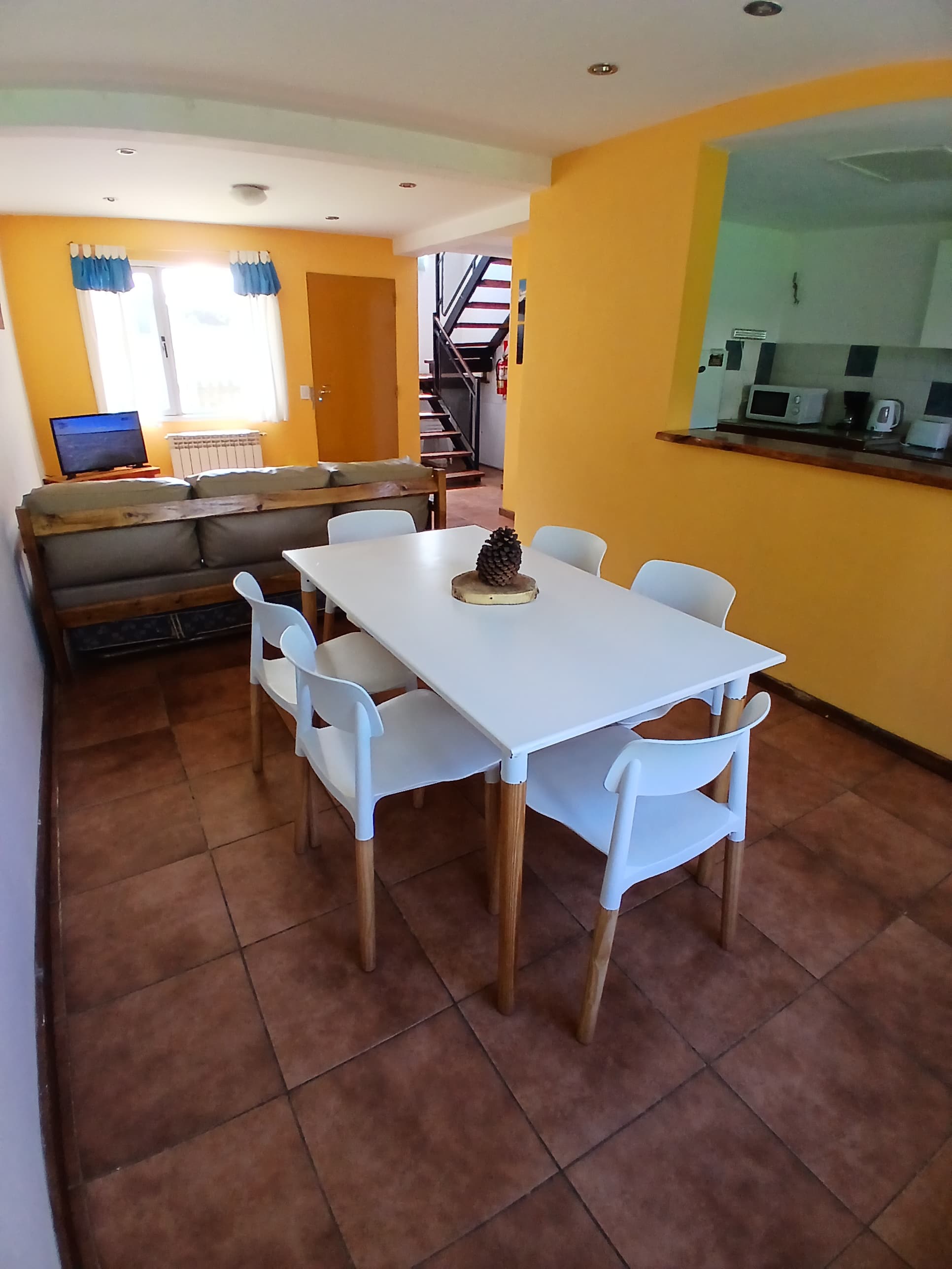 Mesa de comedor blanca con sillas modernas sobre suelo de baldosas y paredes amarillas.