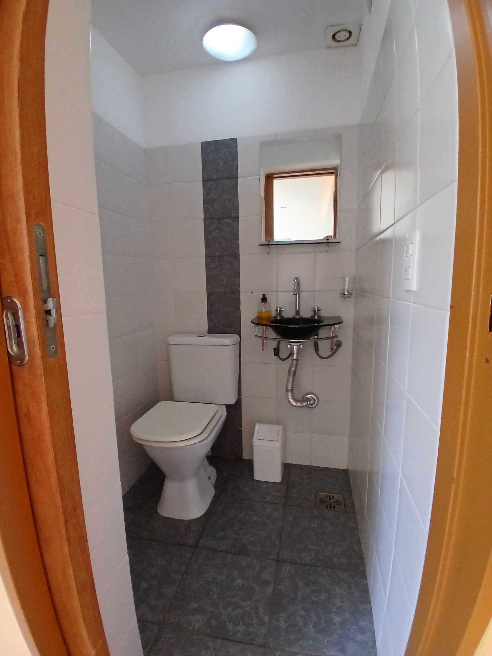 Baño compacto con inodoro blanco, lavabo negro minimalista, azulejos bitono y suelo de baldosas grises.