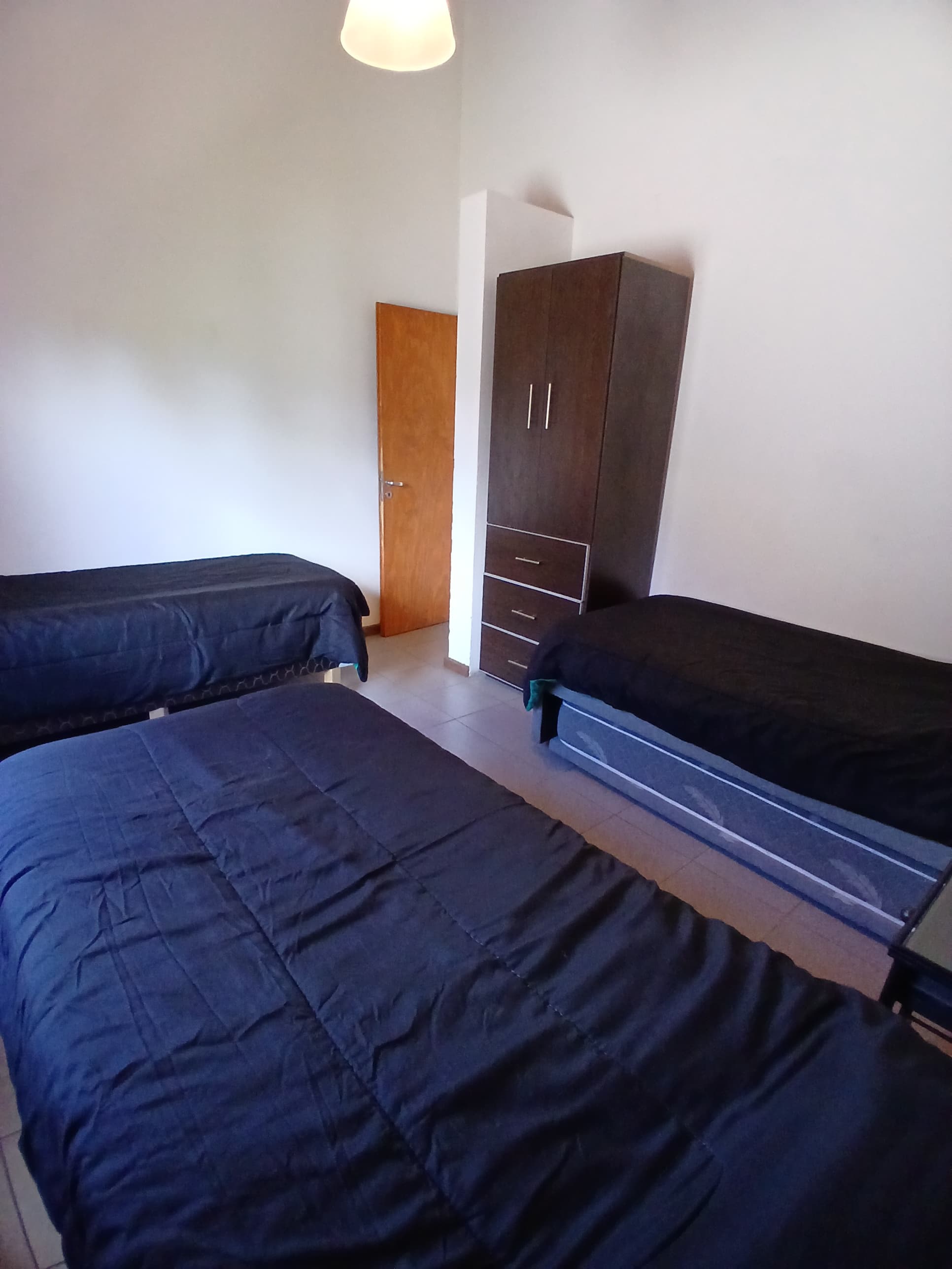 Dormitorio con camas individuales, edredones azul oscuro y un armario de madera marrón oscuro.