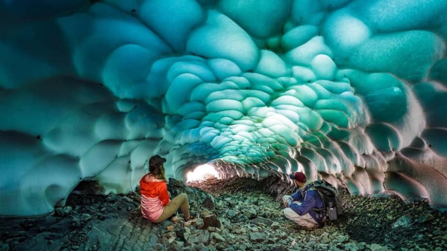 Dos personas observando el techo ondulado de una cueva de hielo azul turquesa brillante.