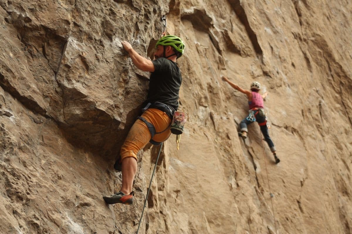 Dos escaladores con cascos ascienden por una pared de roca natural vertical y muy escarpada.